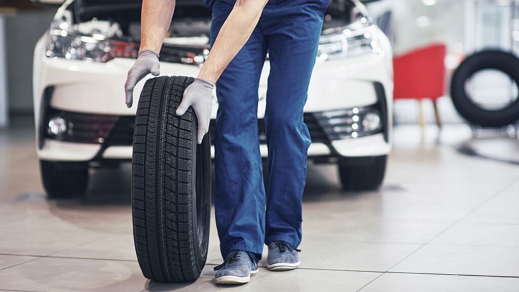 Mechanik w warsztacie trzyma oponę przy samochodzie, przygotowanie do wymiany opon